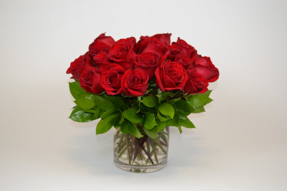 Short arrangement of red roses in a clear glass vase with a compact, rounded shape.