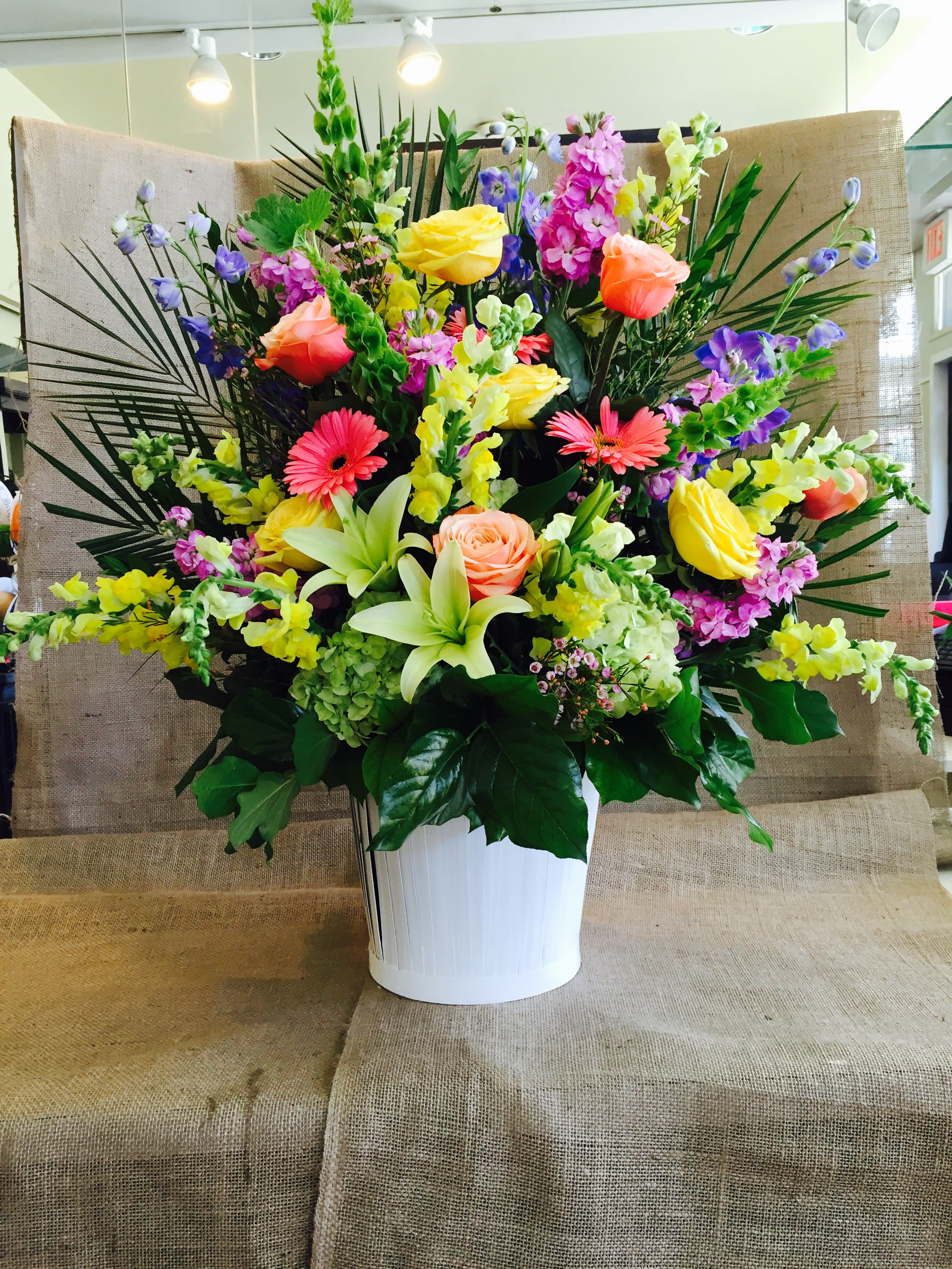 Large mixed bouquet in a white vase with roses, lilies, and bright snapdragons
