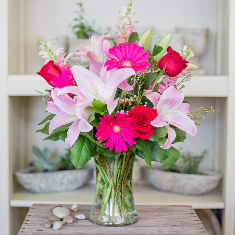 Pink lilies, hot pink gerbera daisies, and red roses in a clear glass vase