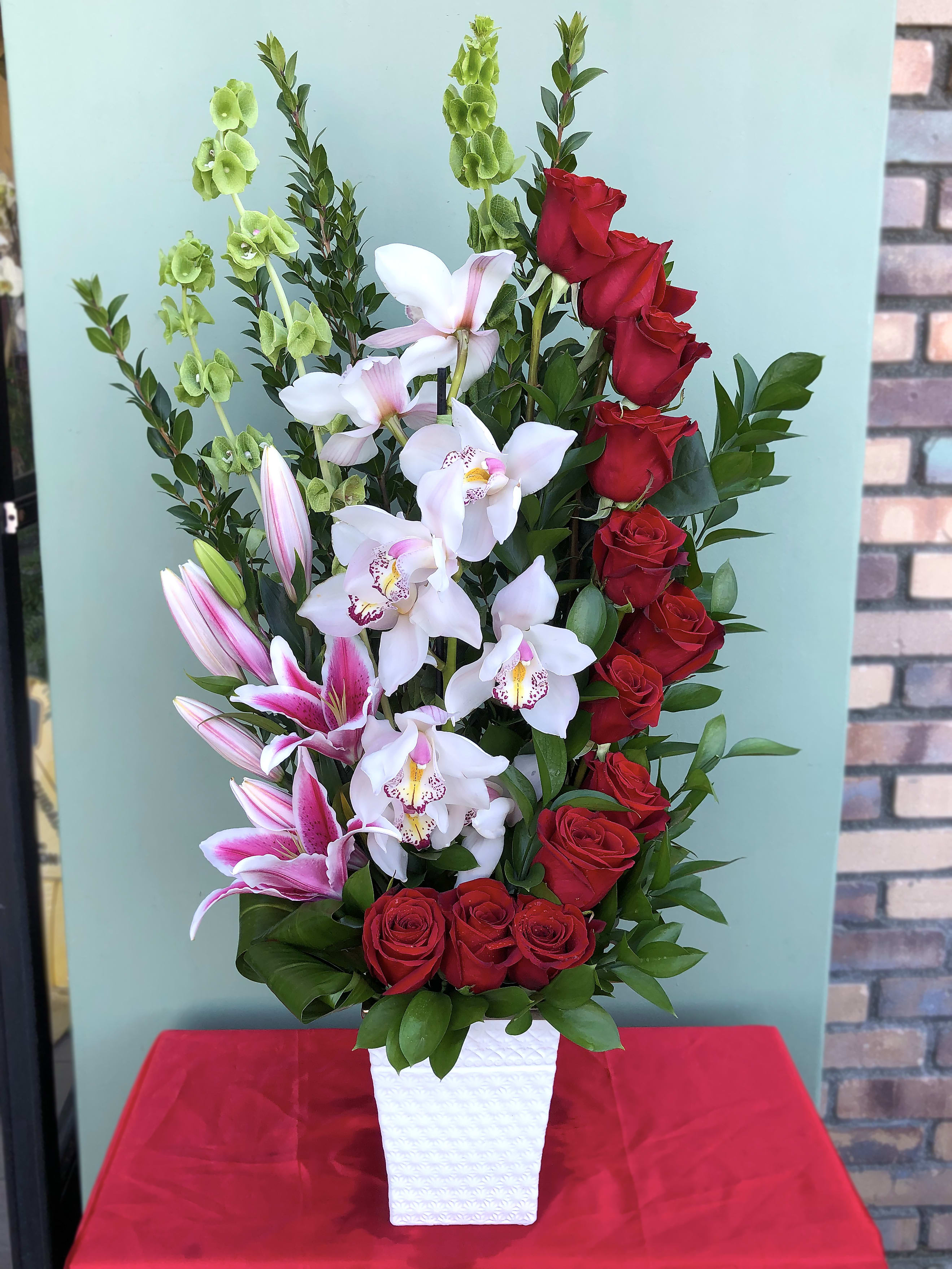 Tall arrangement of red roses, white orchids, and pink lilies in a white vase