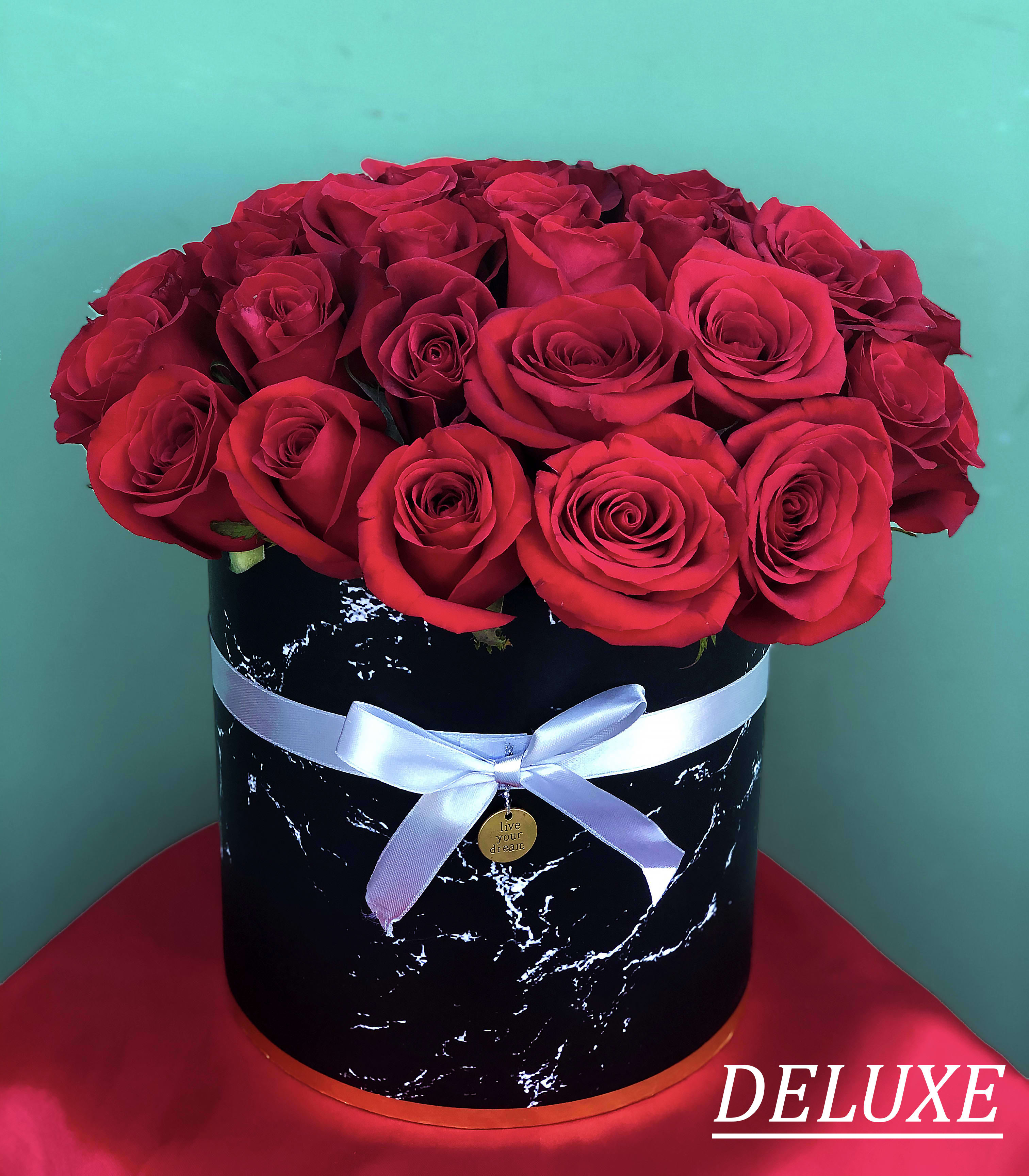 Red roses arranged in a black round box with a white ribbon