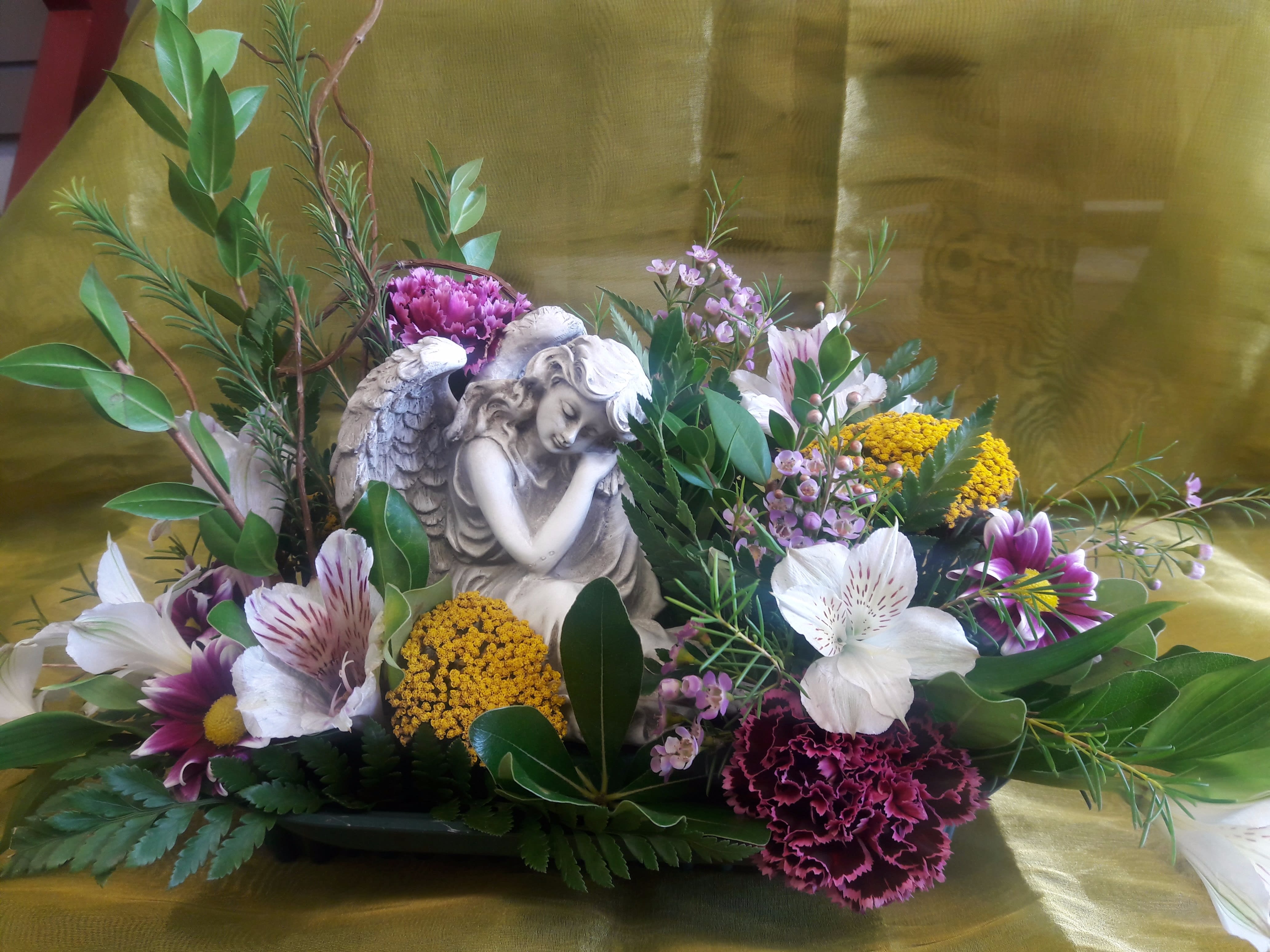 Floral arrangement with an angel figurine and mixed blooms in a low container