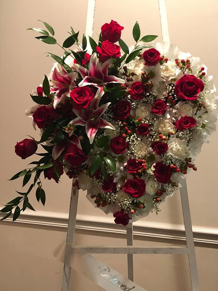 Heart-shaped floral wreath with red roses and white lilies on an easel
