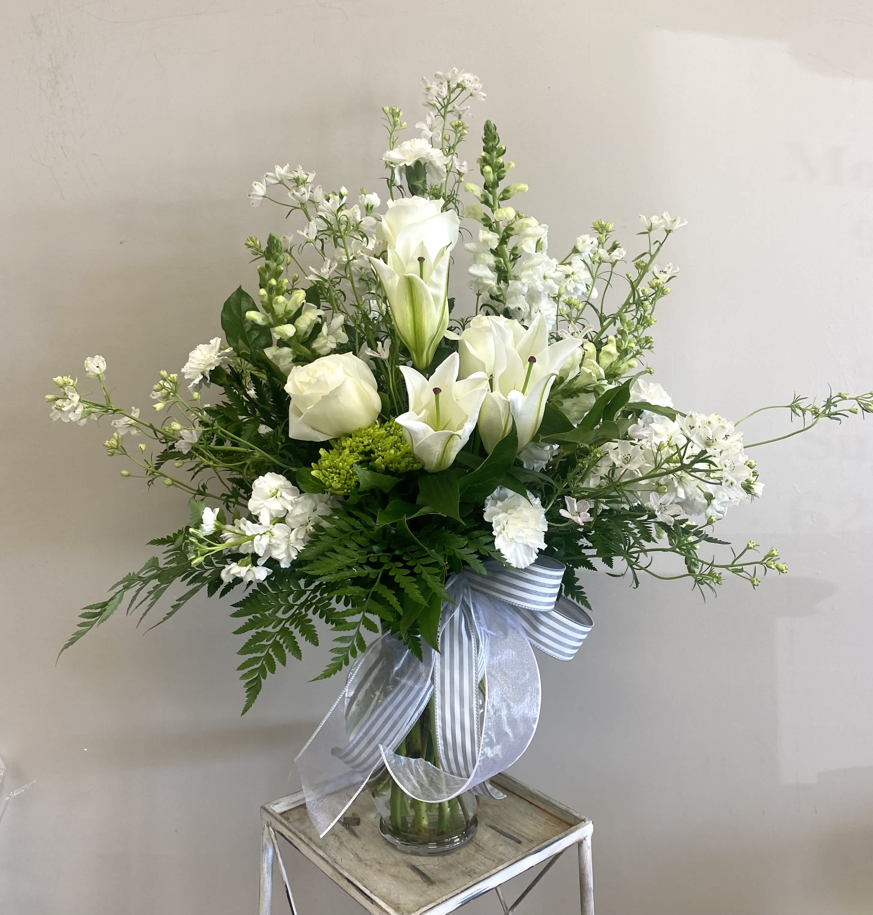 White lilies and roses in a glass vase with a striped ribbon
