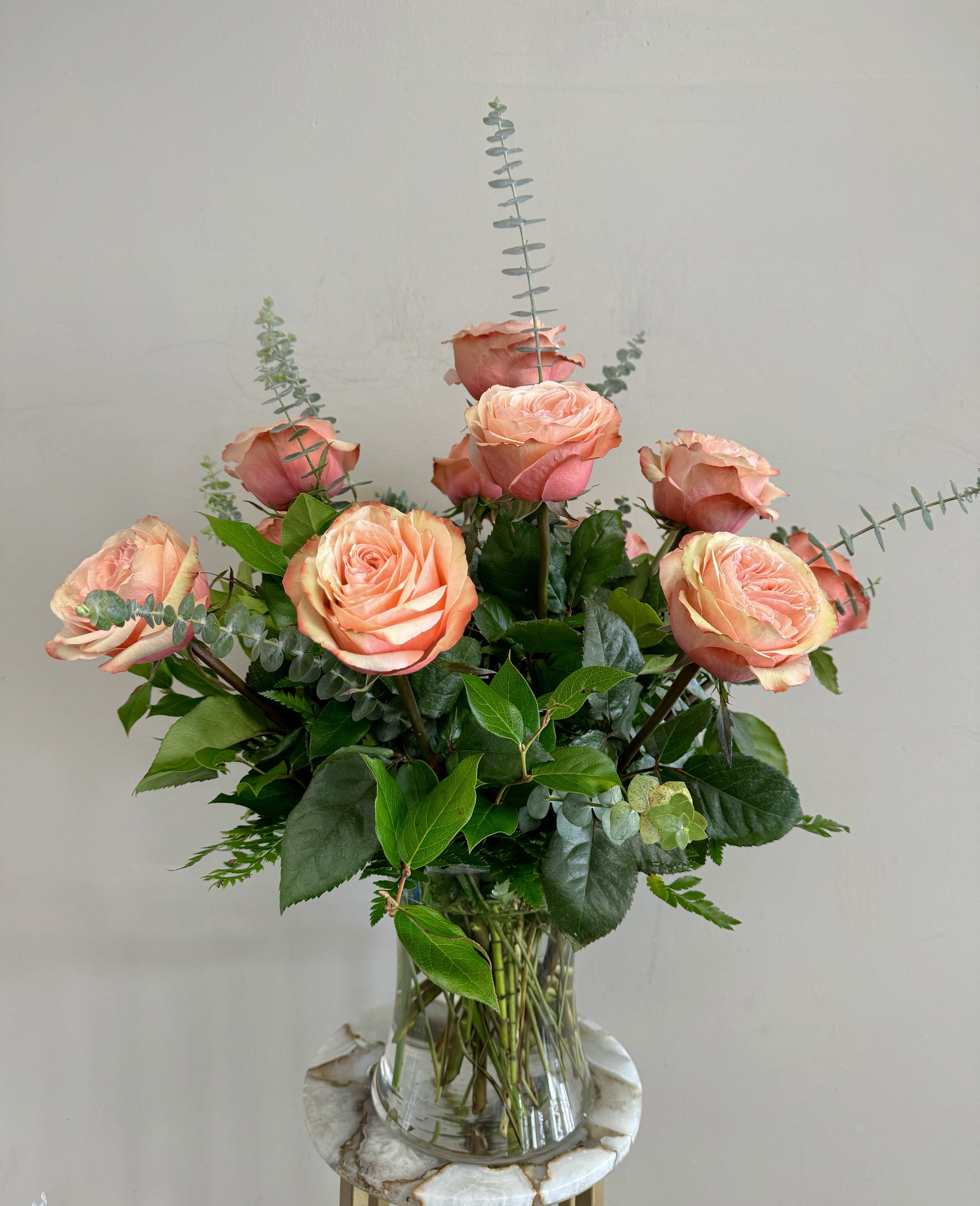 Peach roses arranged in a clear glass vase with greenery.