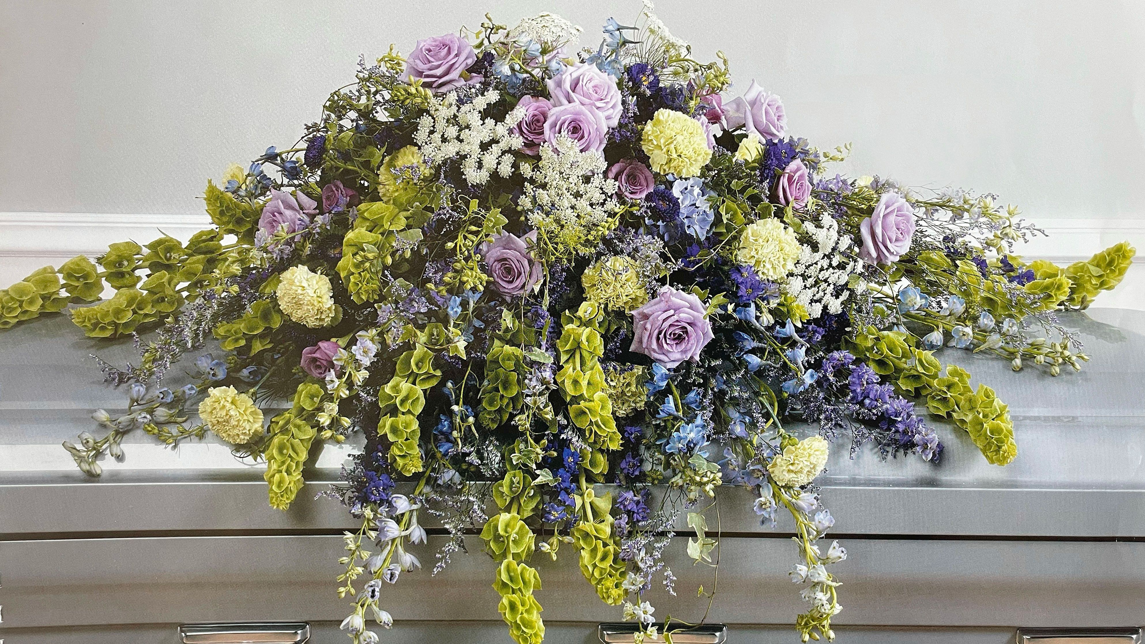 Lavender and blue floral casket spray with trailing greenery
