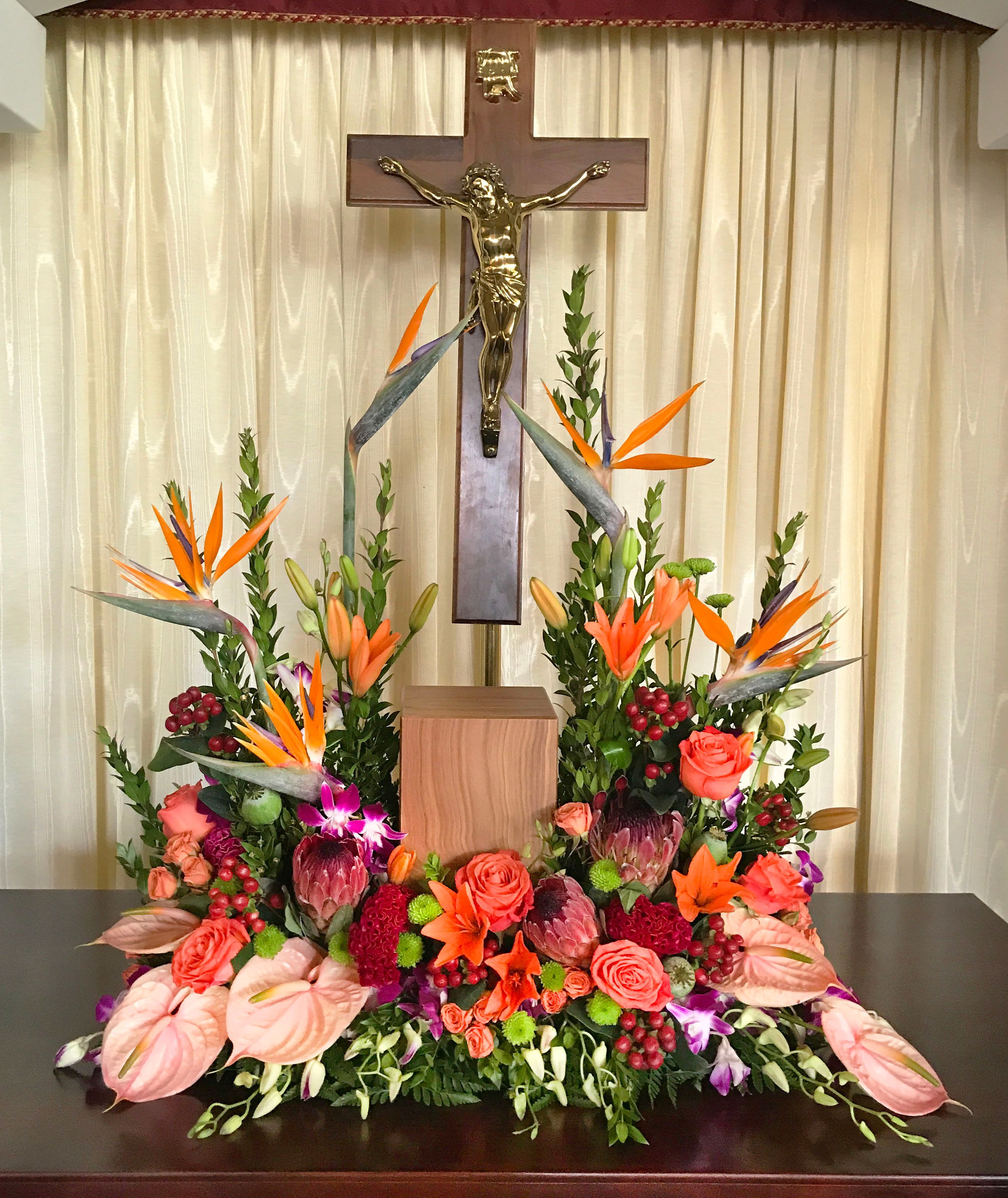 Large floral arrangement with orange birds of paradise and roses beneath a crucifix