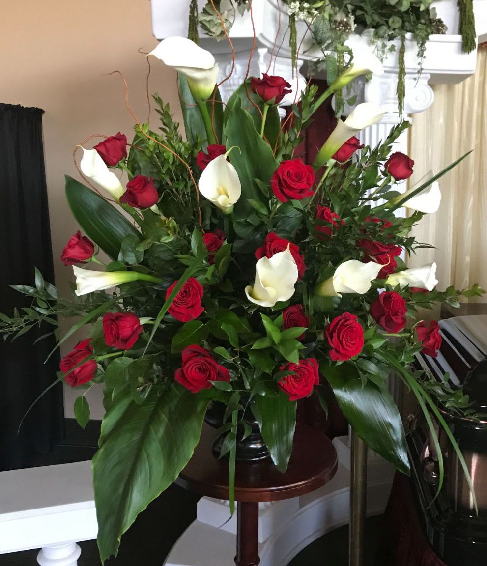 Large arrangement of red roses and white calla lilies in a dark pedestal vase
