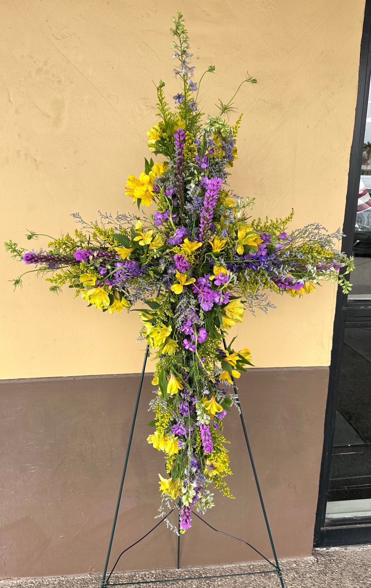 Tall floral cross on an easel with yellow and purple flowers