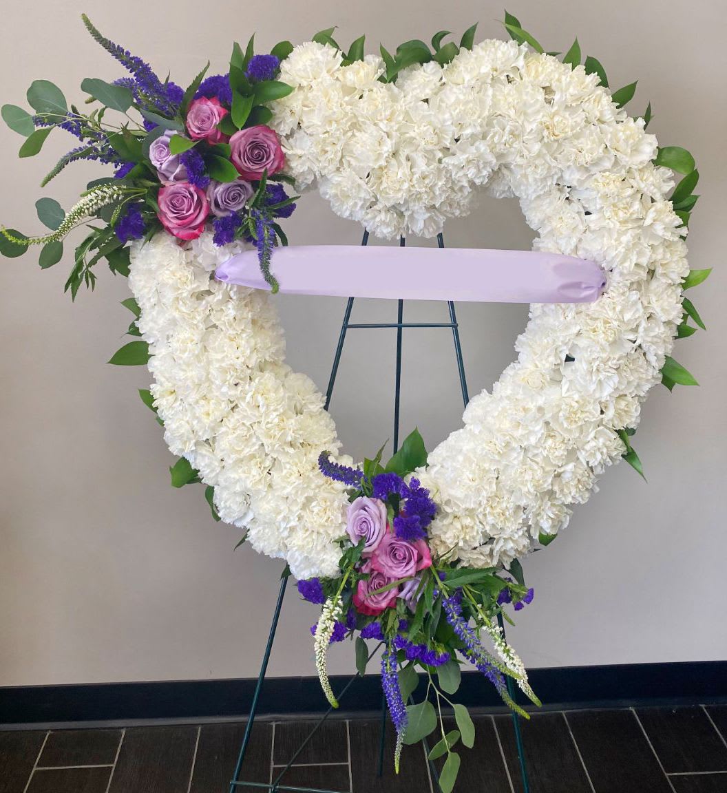 Heart-shaped white floral wreath with pink and purple roses on an easel