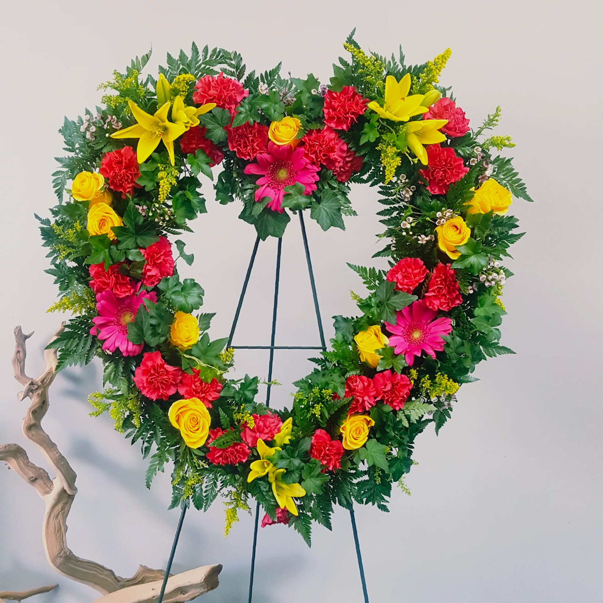 Heart-shaped floral wreath on a stand with red, yellow, and pink flowers
