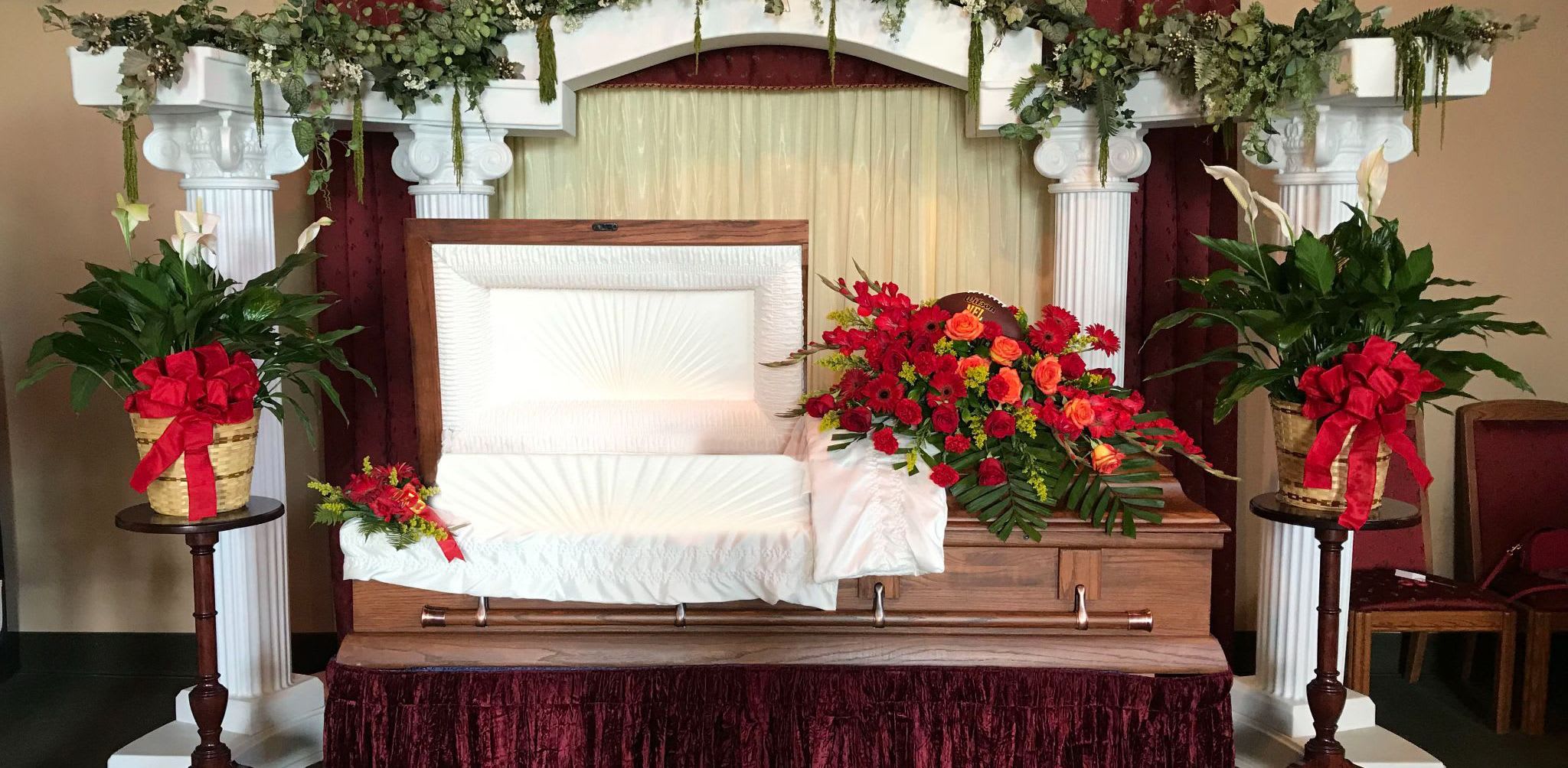 Casket spray with red and orange flowers beside matching potted plants
