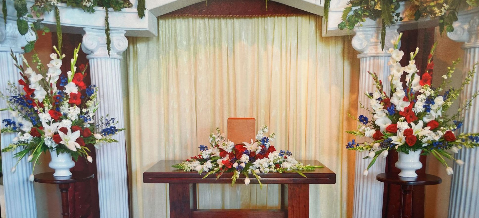 Symmetrical floral altar display with red, white, and blue flowers in white urns