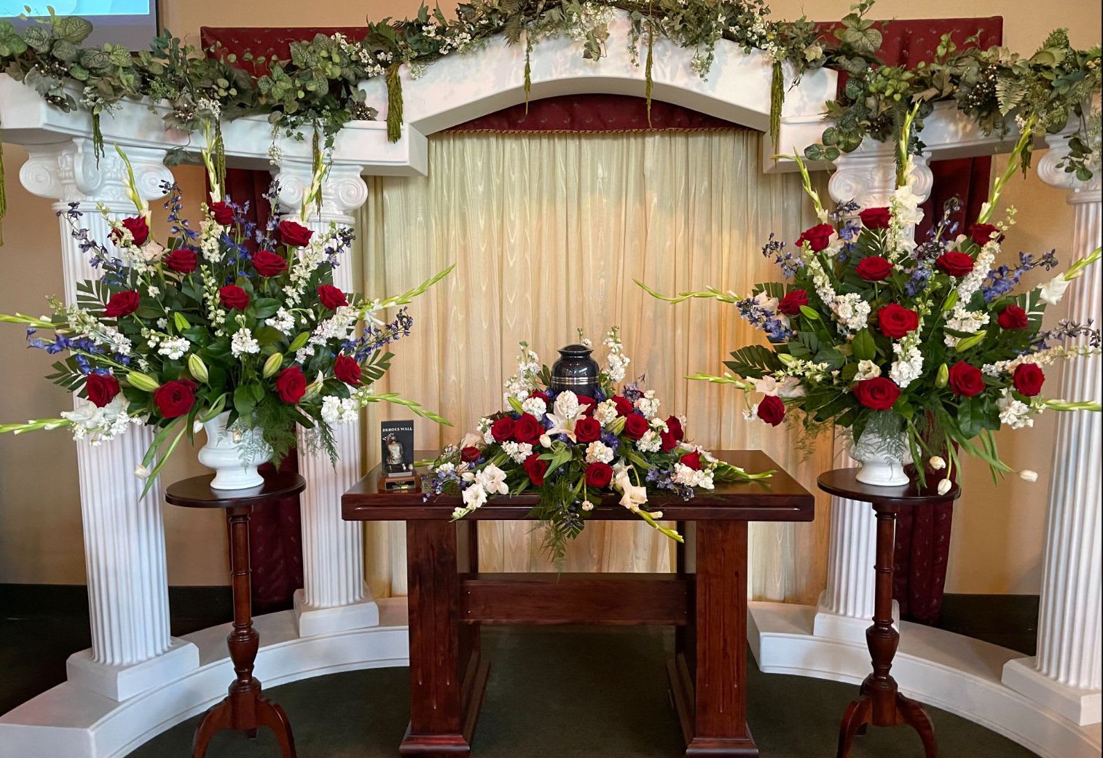 Symmetrical funeral floral display with red and white arrangements on pedestals and a table centerpiece