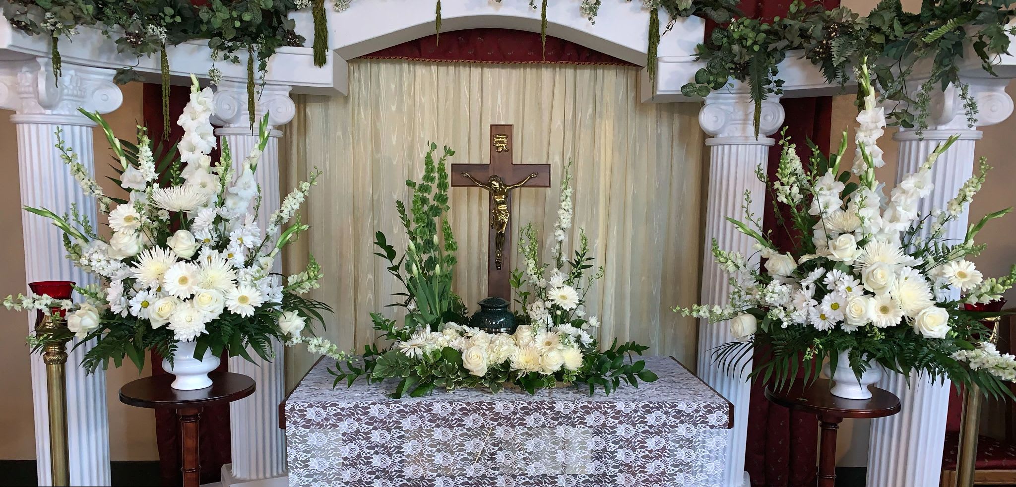 White floral funeral altar with tall arrangements and a crucifix