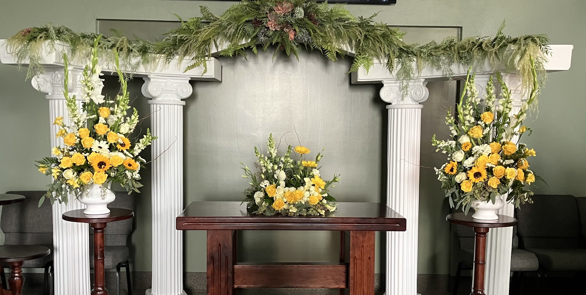Yellow and white floral arrangements on pedestals beneath a white arch.