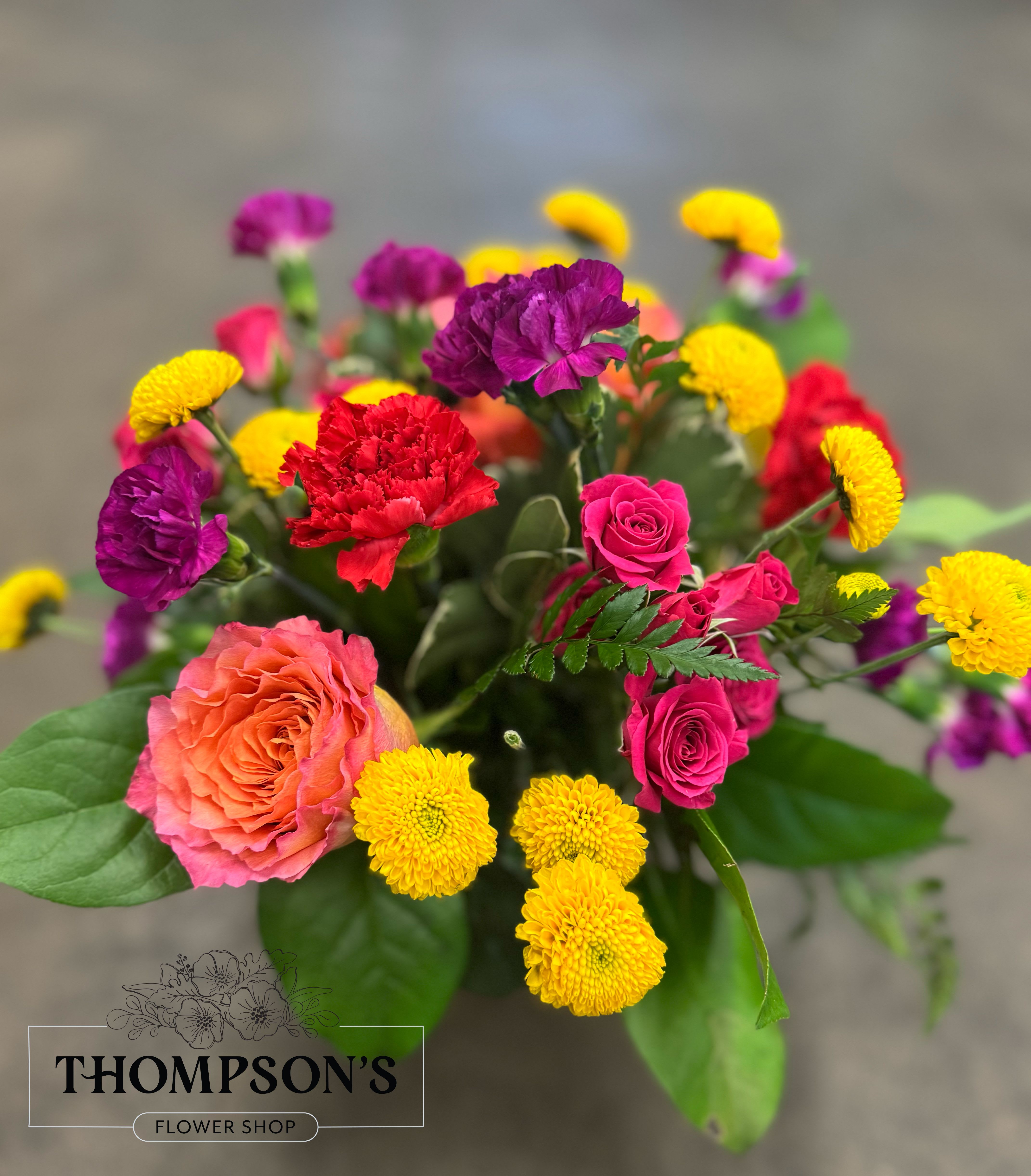 Goodyear Glow - Bursting with color and personality, this cheerful bouquet radiates warmth and joy. Featuring bold yellow button mums, hot pink spray roses, purple and red carnations, and sunset-hued roses, it’s designed to brighten any day. Whether you’re sending birthday wishes, congratulations, or a dose of cheer, Goodyear Glow delivers sunshine in every stem.