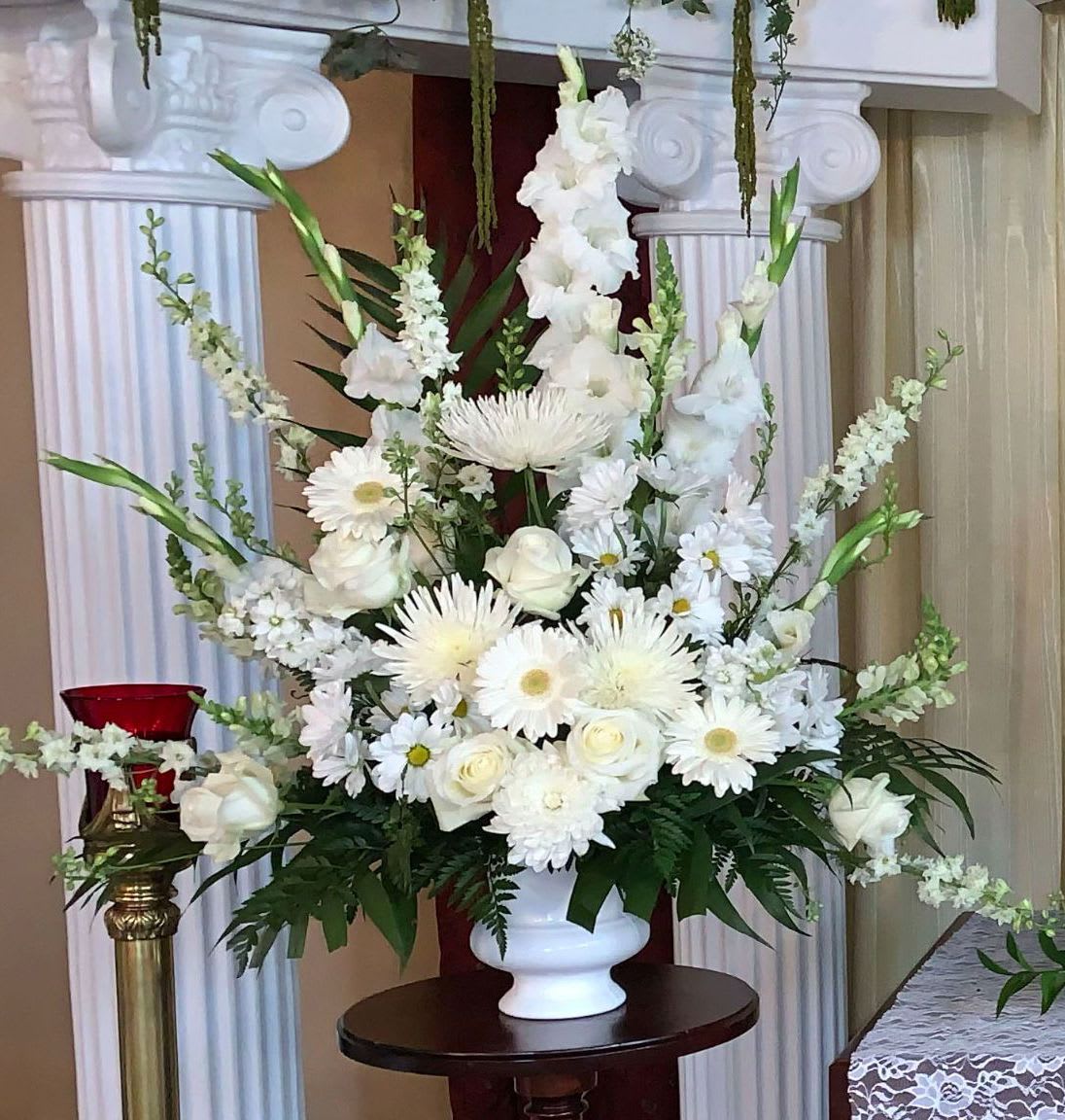 Large all-white arrangement of roses, daisies, and mums in a white pedestal vase