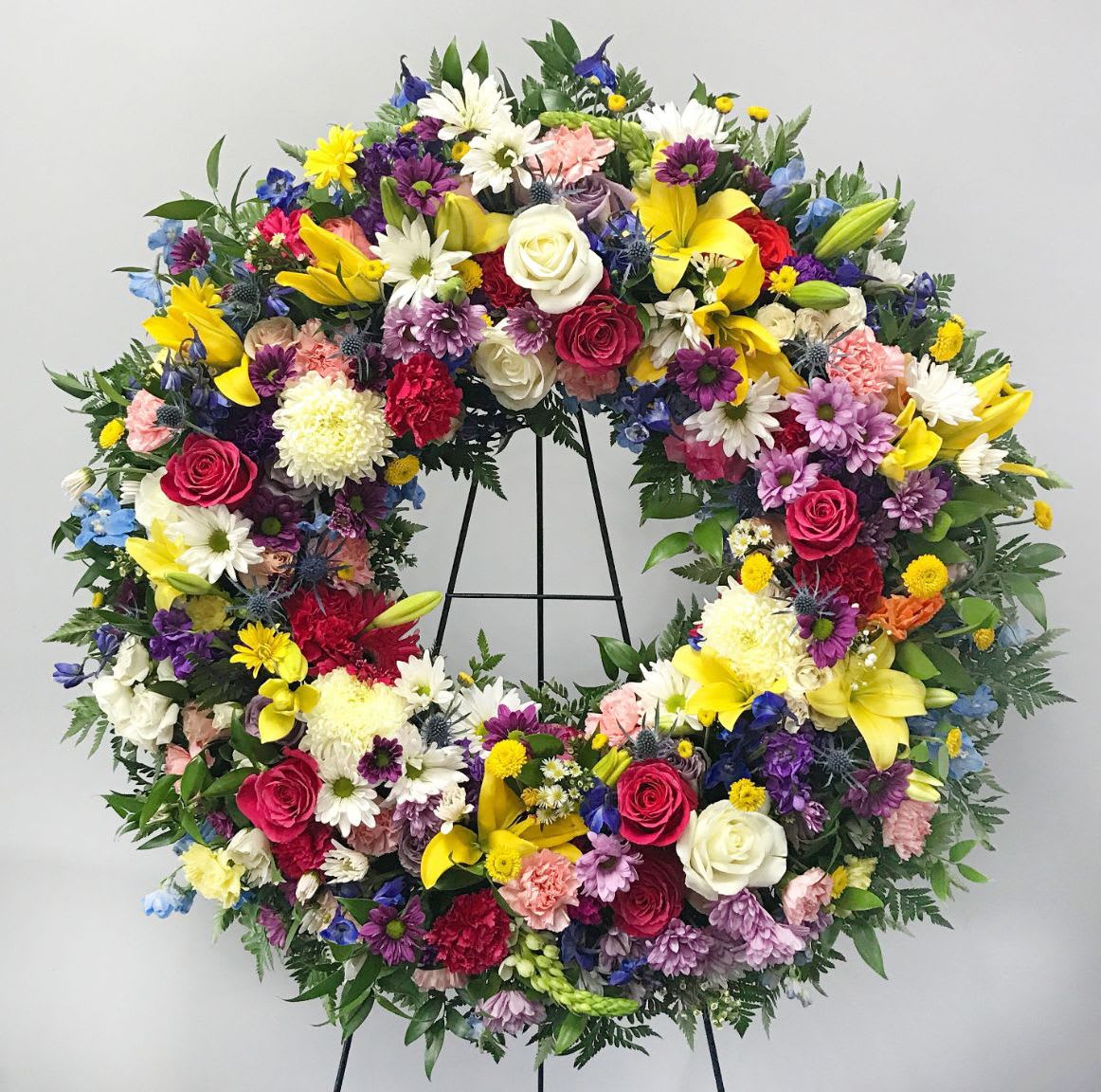 Large circular floral wreath with mixed colorful flowers on a stand