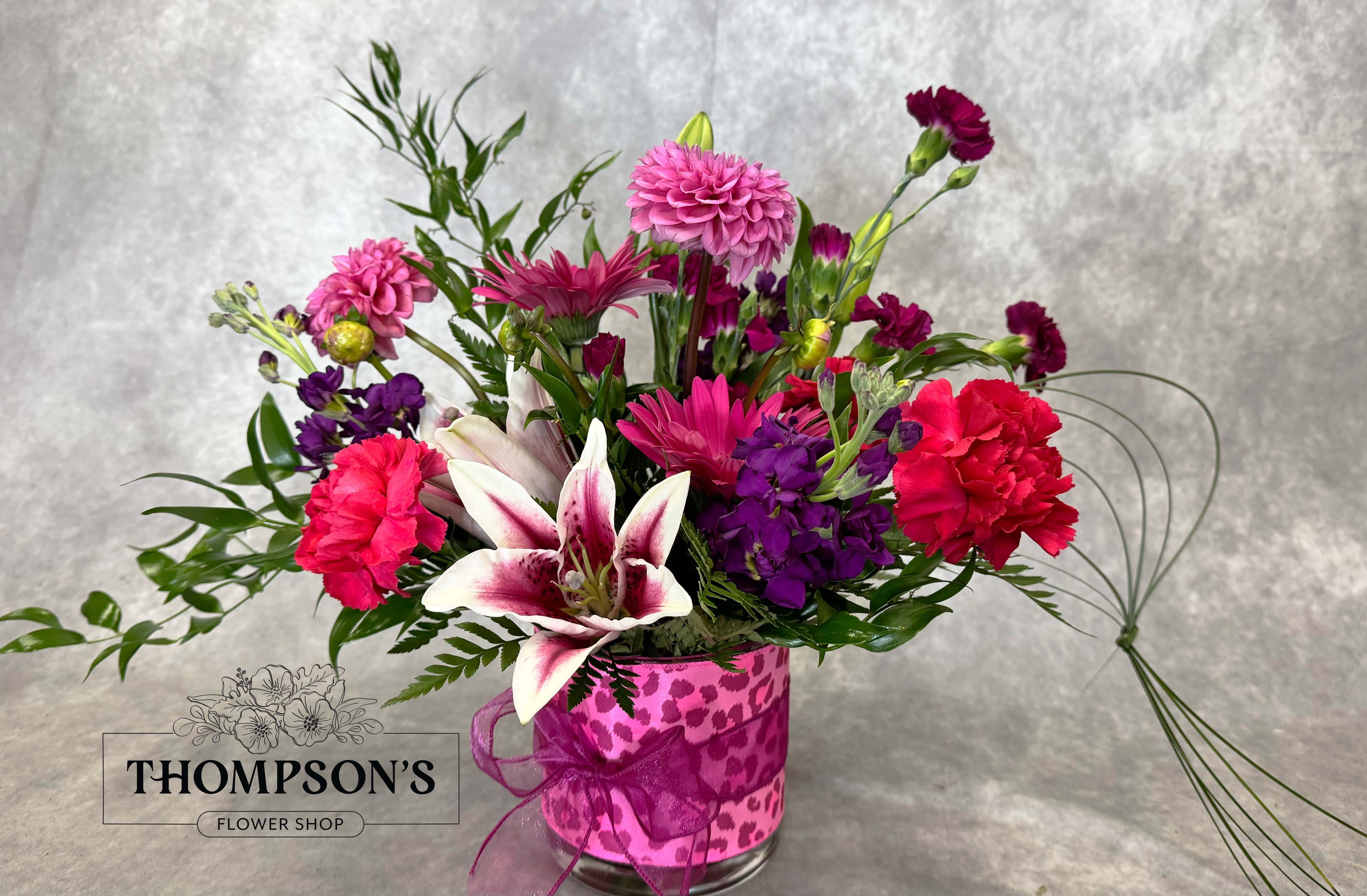 Mixed pink and purple bouquet in a clear glass vase with a ribbon