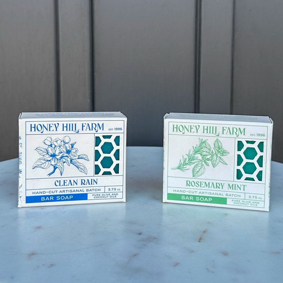 Two Honey Hill Farm bar soap boxes, Clean Rain and Rosemary Mint, on a light stone surface