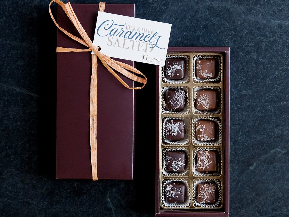 Rectangular gift box of salted caramels with ribbon and open tray showing assorted chocolates.