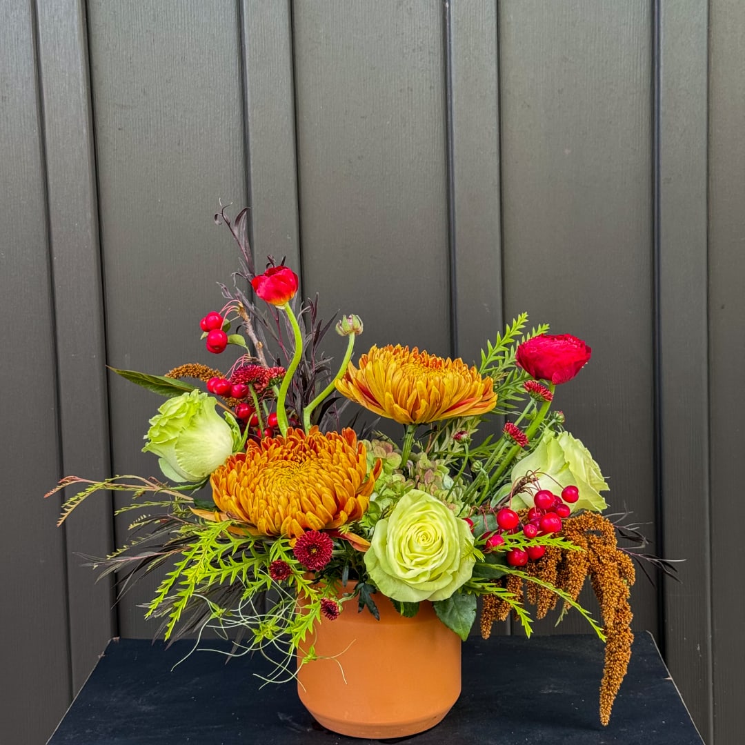 Colorful floral arrangement in an orange pot with red, yellow, and green blooms
