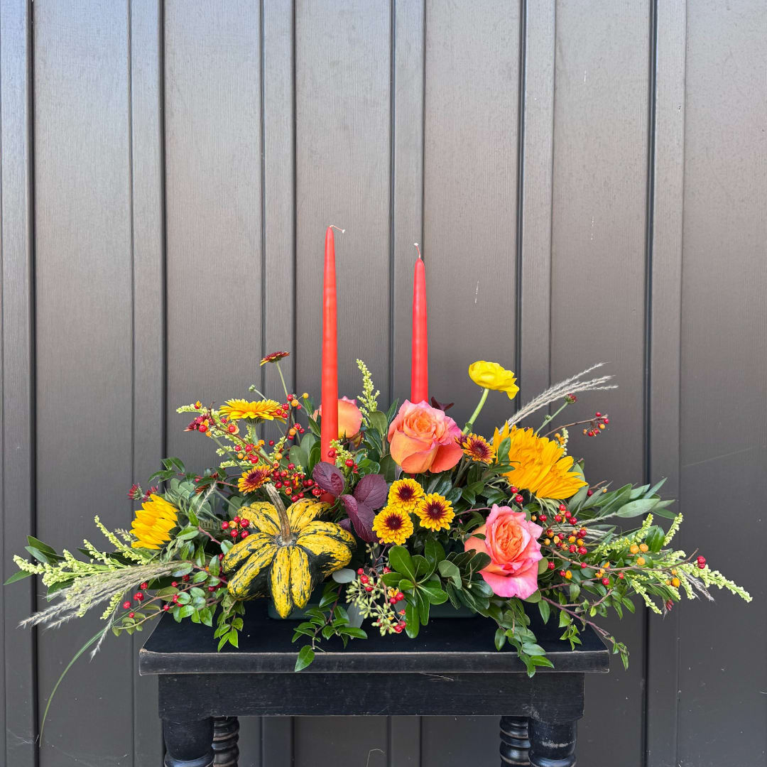 Autumn floral arrangement with roses, chrysanthemums, and two red taper candles