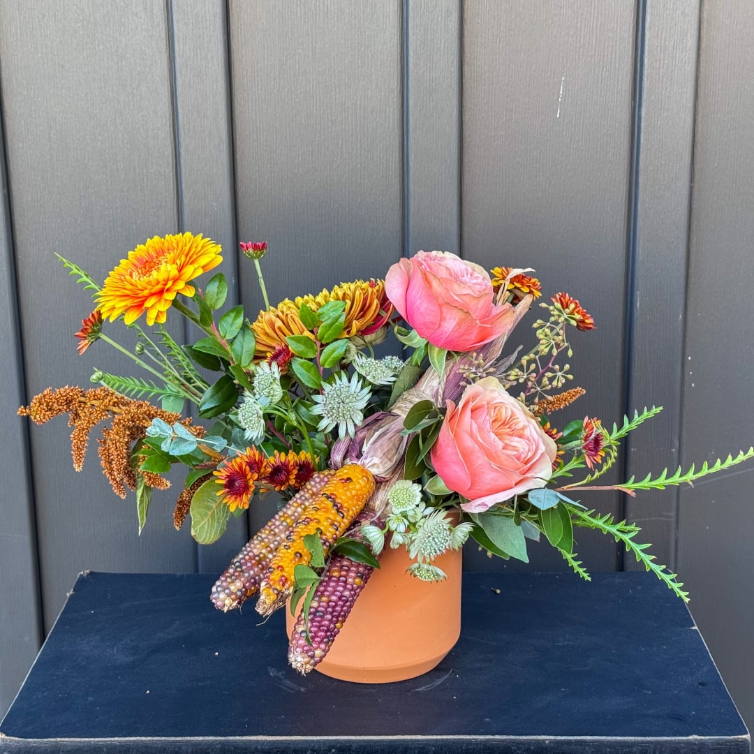 Mixed bouquet with pink roses and orange-yellow blooms in a terracotta vase