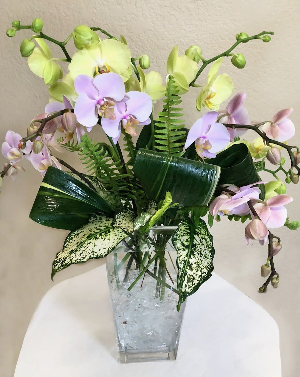 Orchid arrangement in a clear square vase with broad leaves