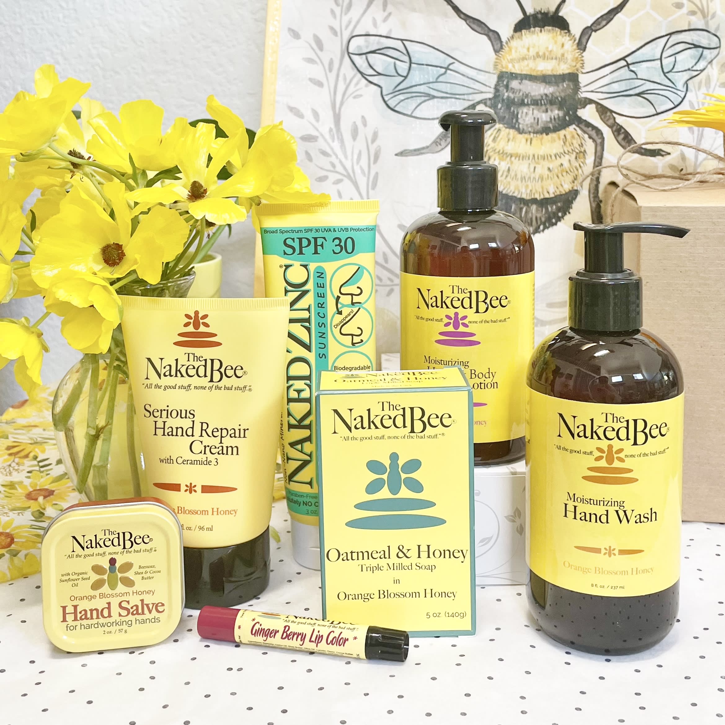 Yellow flowers in a vase beside assorted Naked Bee bath and body products