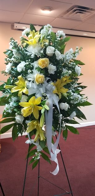Standing floral spray with yellow lilies, white roses, and a white ribbon