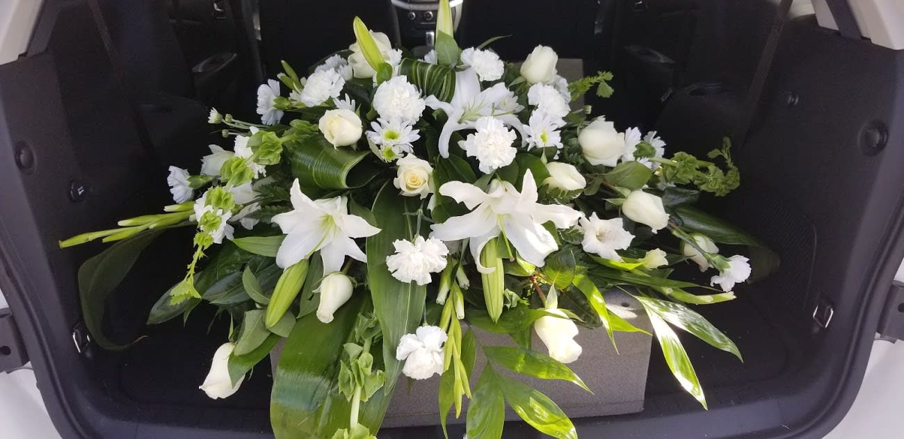 White floral casket spray with lilies, roses, and carnations