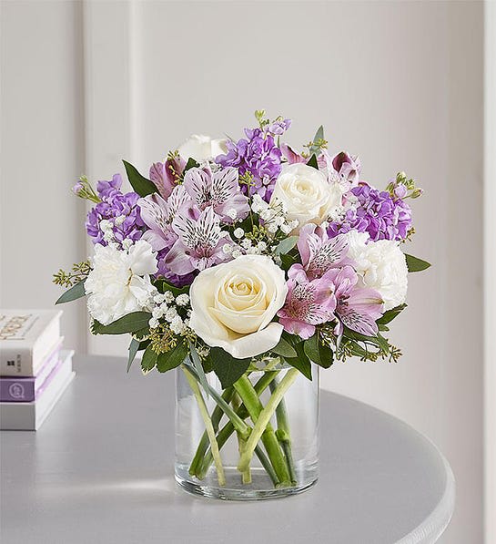 Bouquet of white roses, purple blooms, and pink lilies in a glass vase