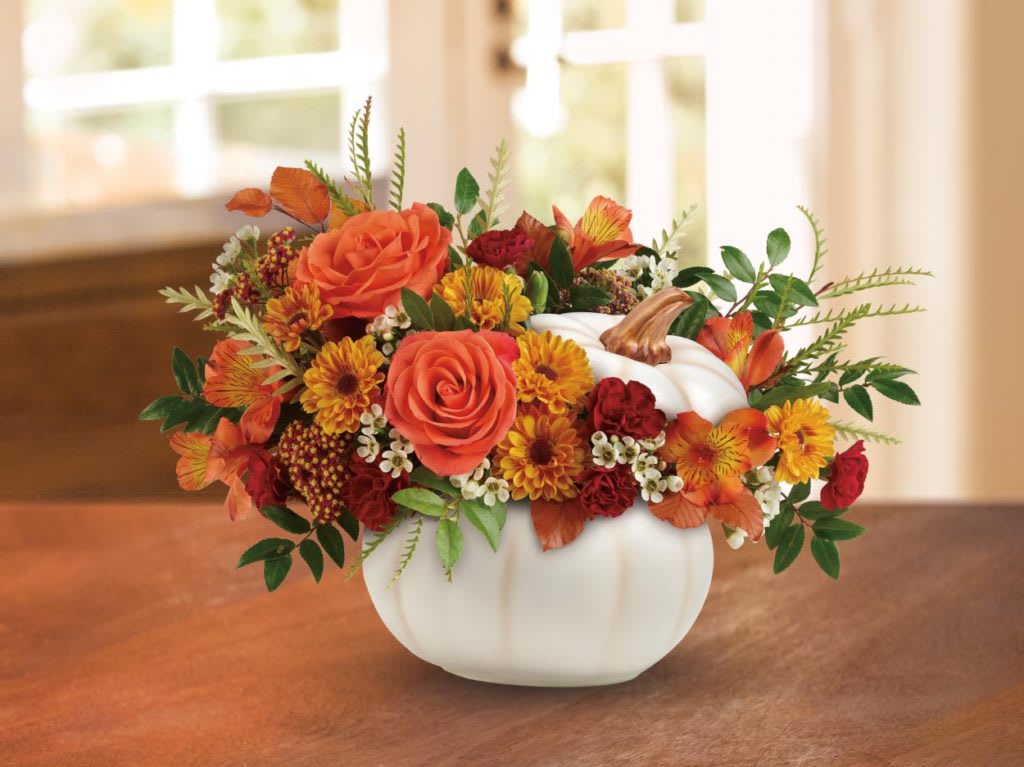 Orange and red floral arrangement in a white pumpkin vase