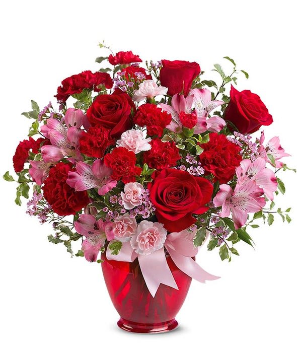 Red roses and pink flowers arranged in a red vase with a pink ribbon