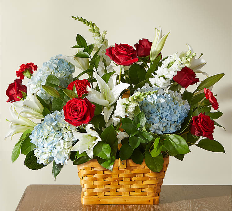 Basket arrangement of red roses, blue hydrangeas, and white lilies