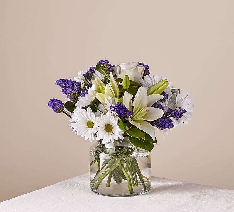 White lilies and daisies in a clear glass vase with purple filler flowers