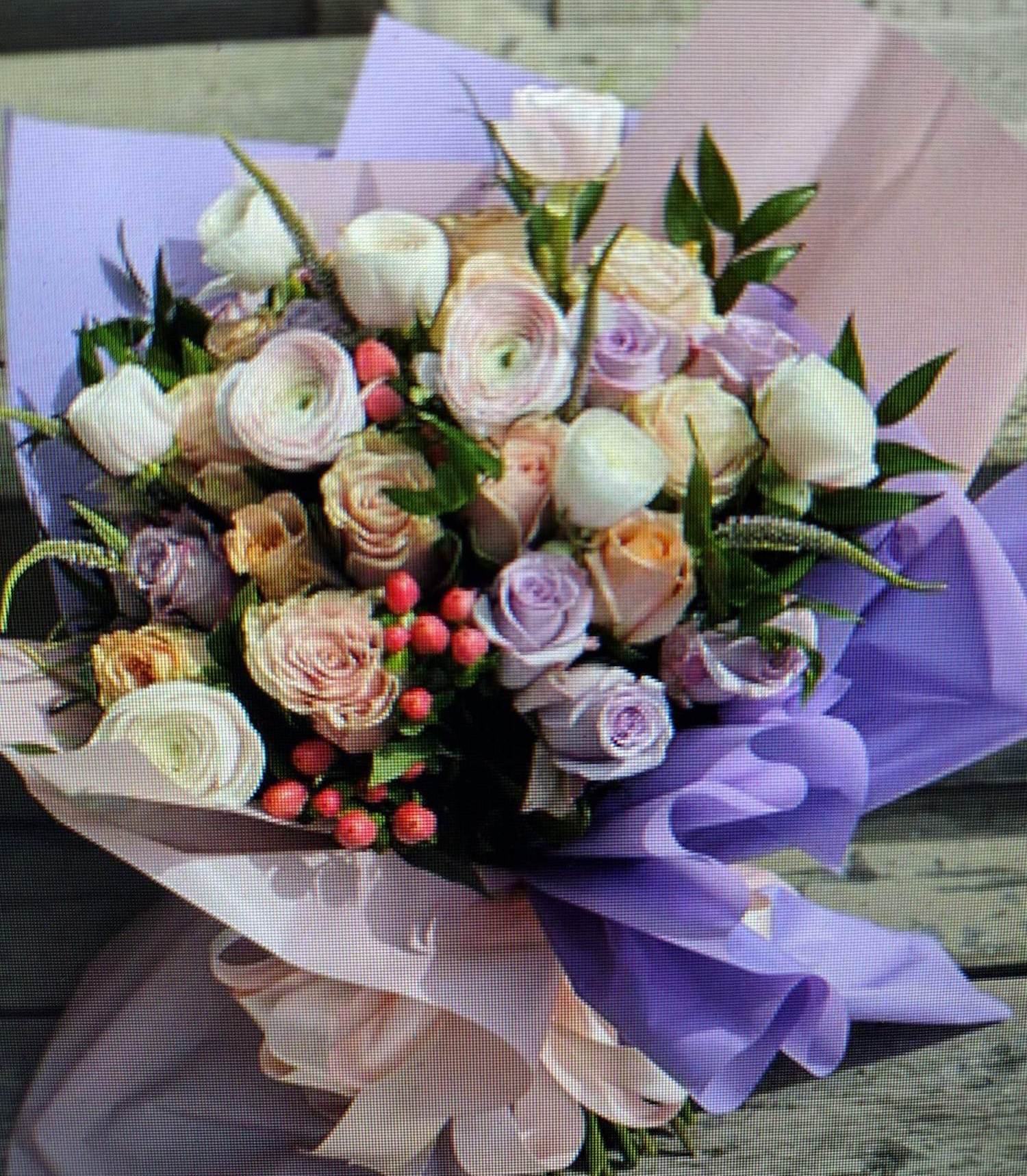 Pastel bouquet of roses and ranunculus wrapped in lavender paper
