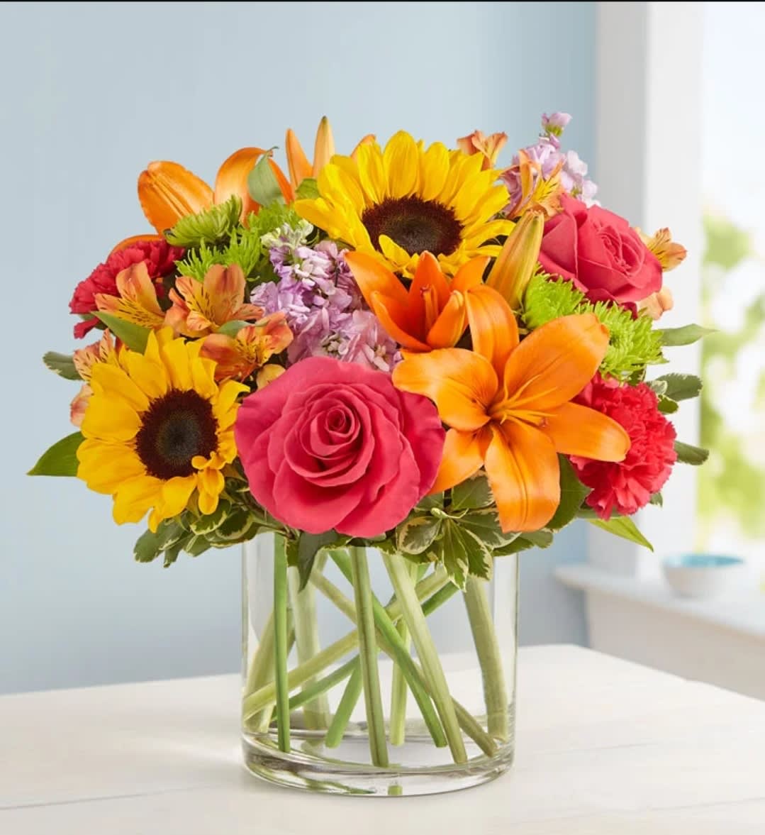Bright mixed bouquet with sunflowers, roses, lilies, and carnations in a clear glass vase