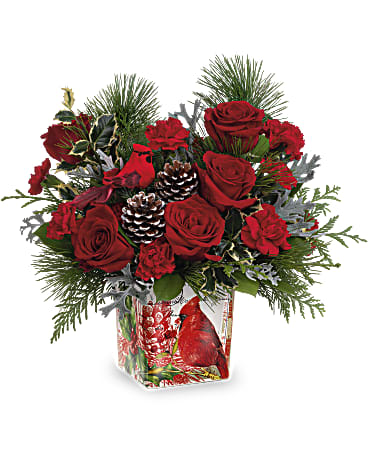 Red roses and carnations in a glass vase with pinecones and evergreen accents