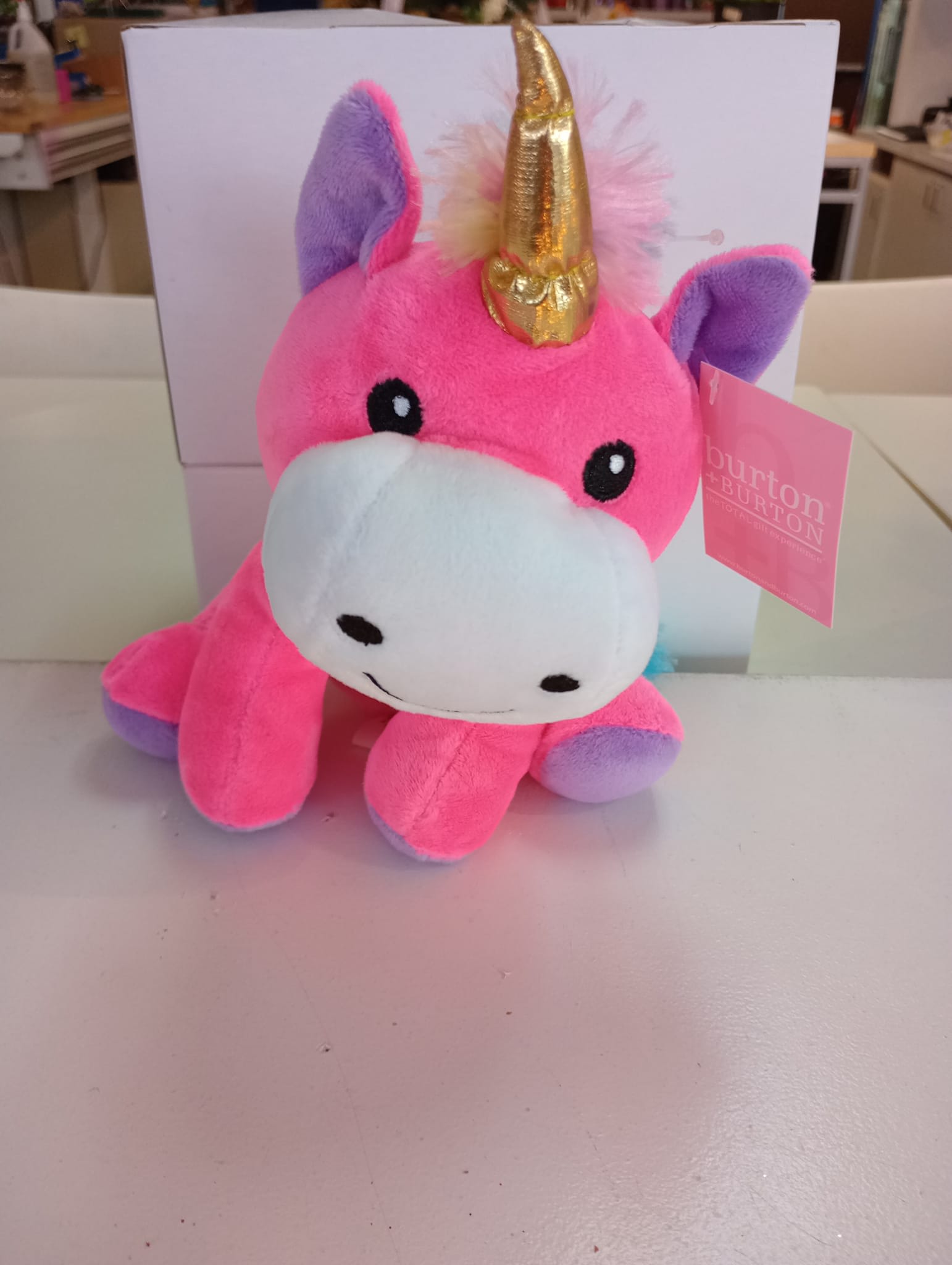 Pink plush unicorn toy with a gold horn and purple ears