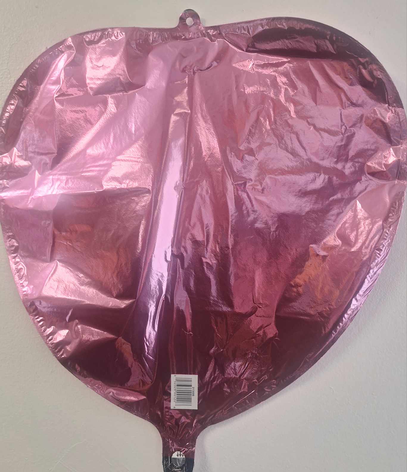 Pink metallic heart-shaped balloon against a plain wall