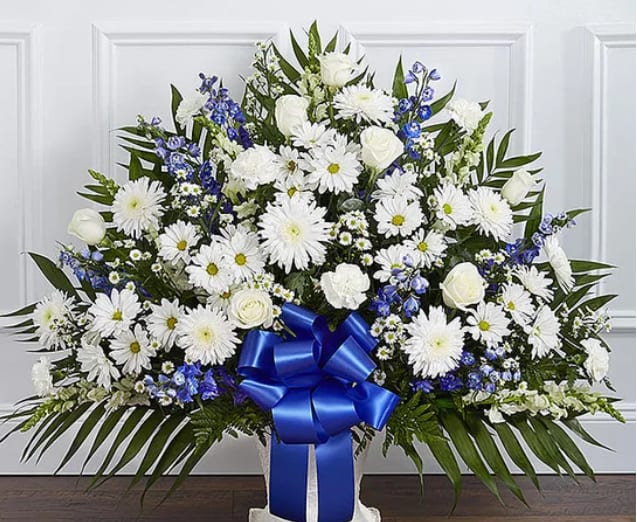 White floral standing spray with blue ribbon and daisies