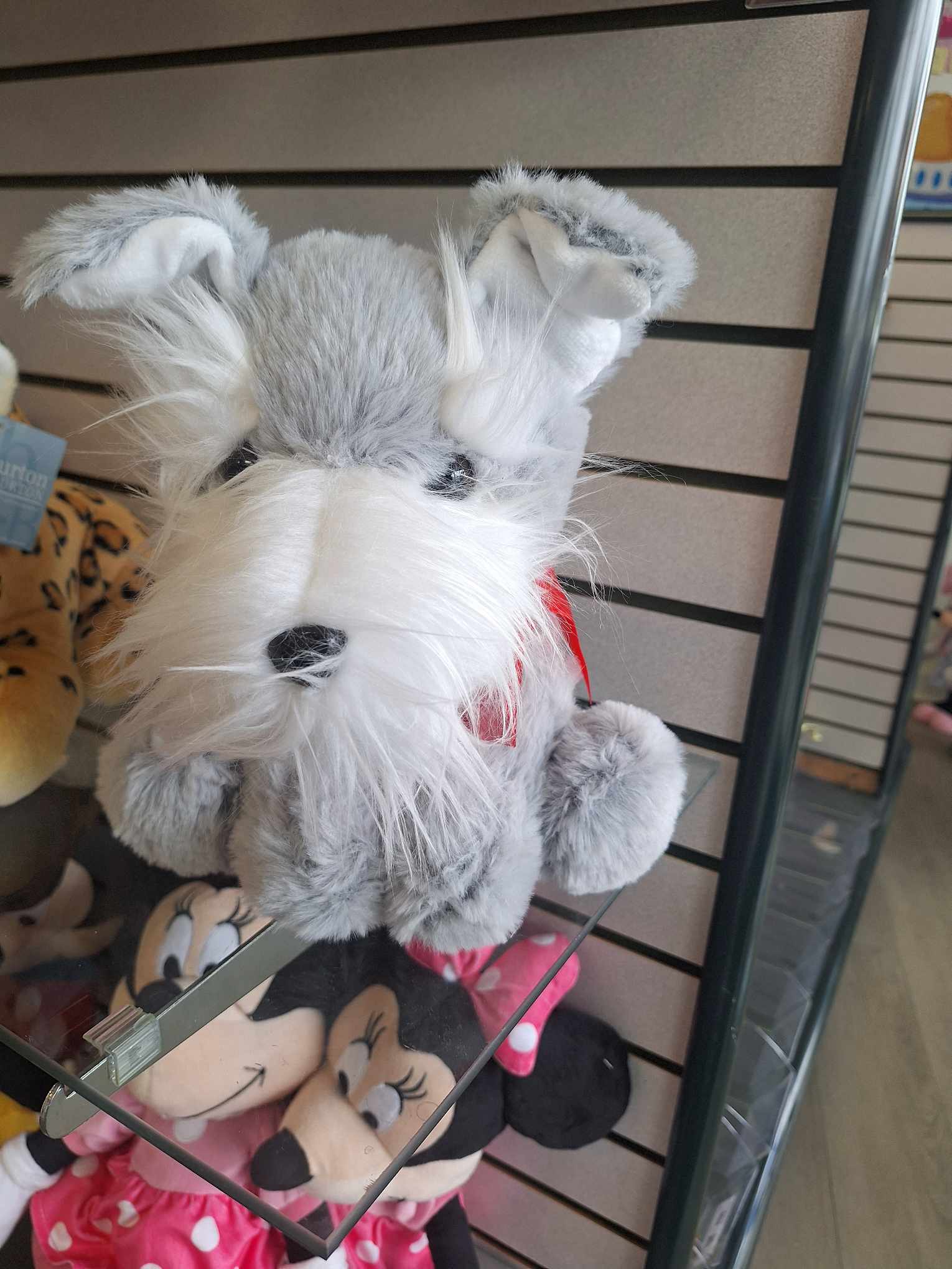 Gray and white plush dog toy with a red scarf on a store shelf