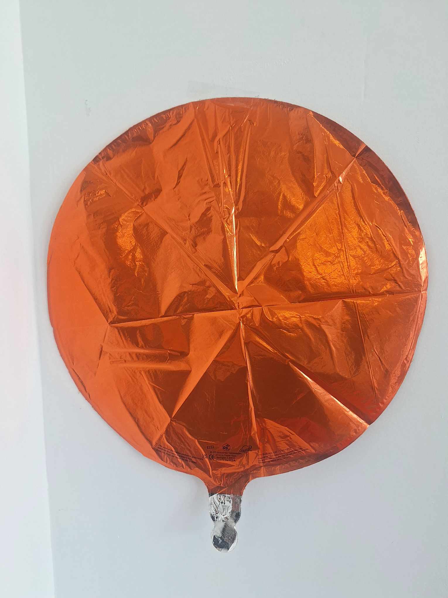 Orange round foil balloon against a white wall