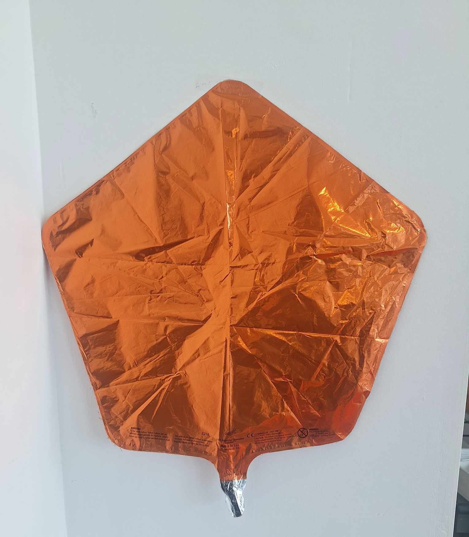 Orange metallic foil balloon shaped like a leaf or kite
