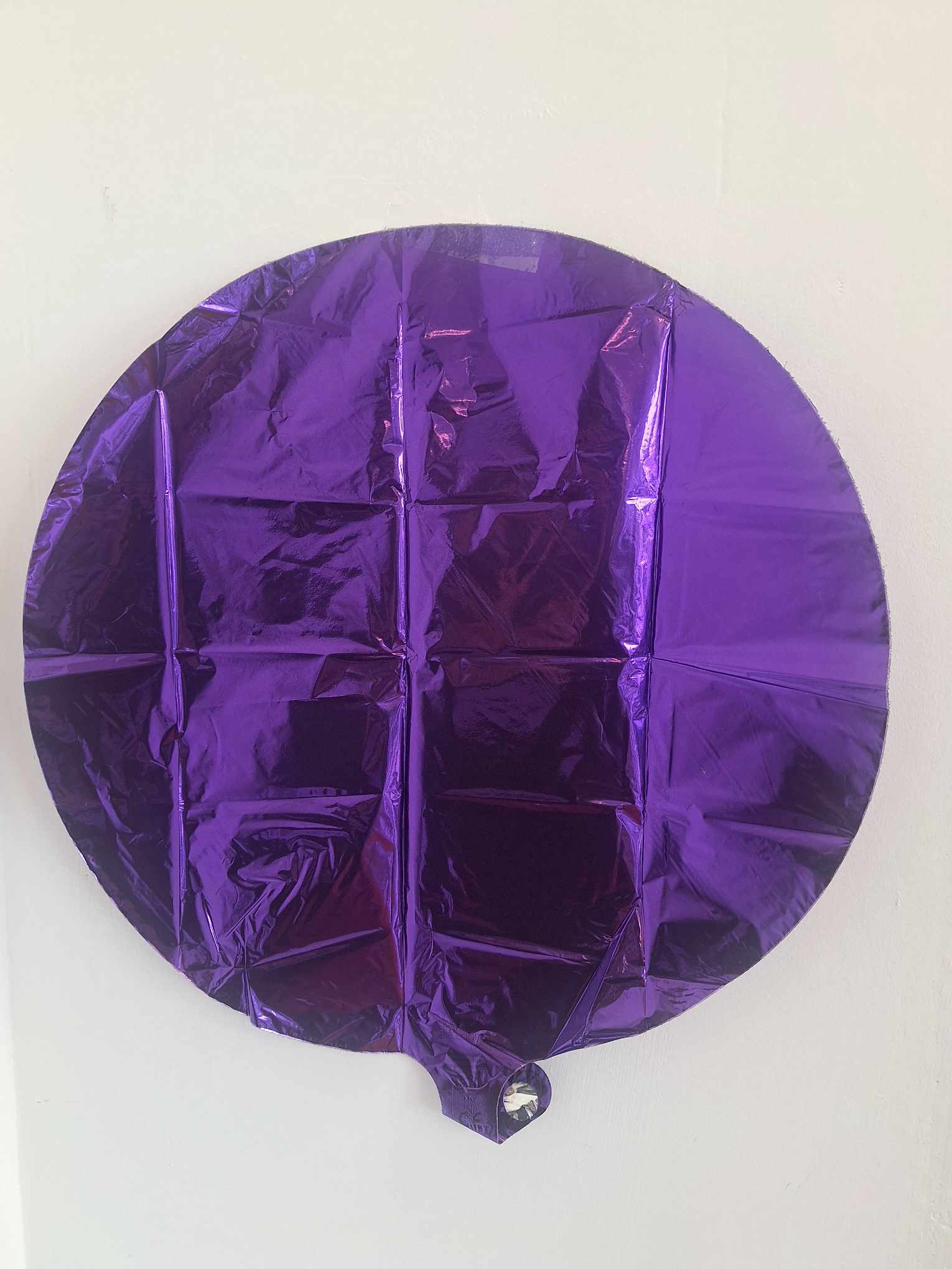 Purple round foil balloon against a white wall