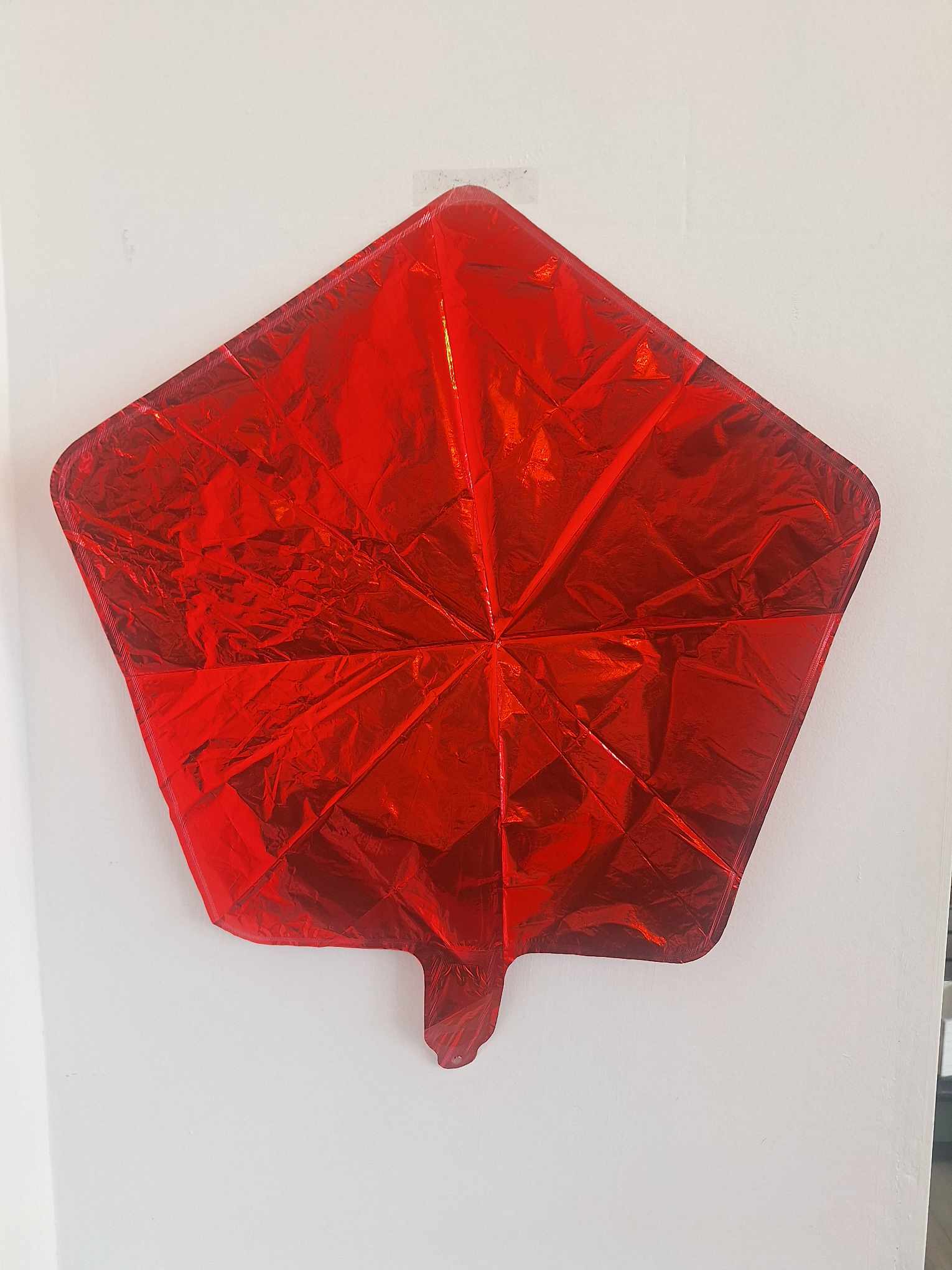 Red star-shaped foil balloon on a white wall