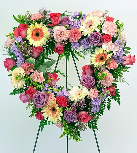 Heart-shaped floral wreath on a stand with pink, purple, and yellow blooms